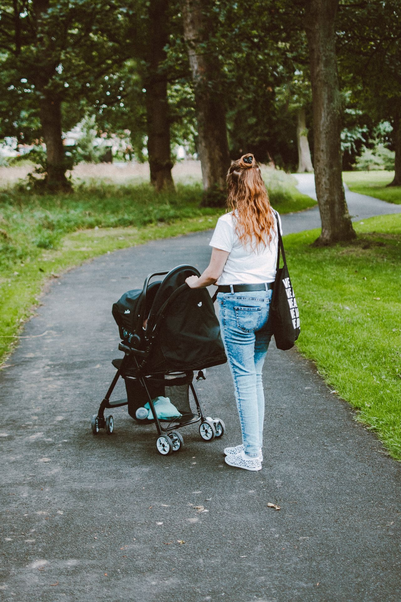 An adult pushing a stroller along a tree-lined park path