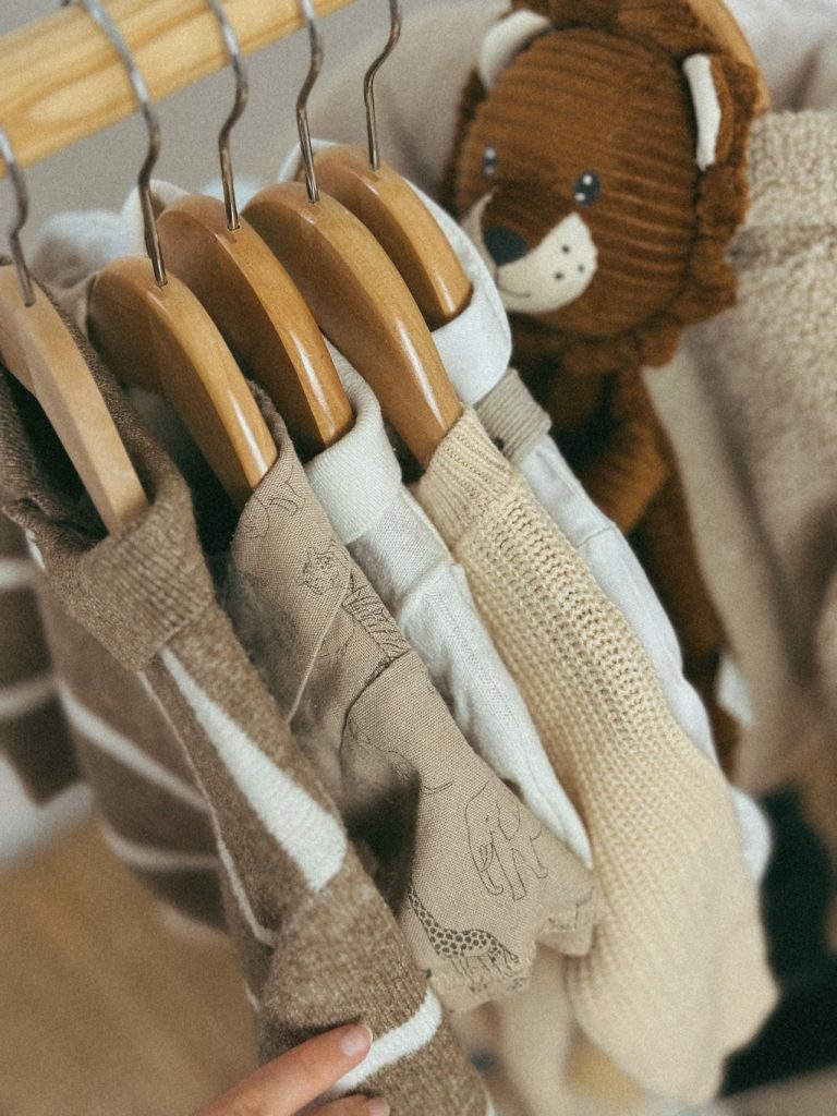 Baby clothes on wooden hangers beside a soft toy