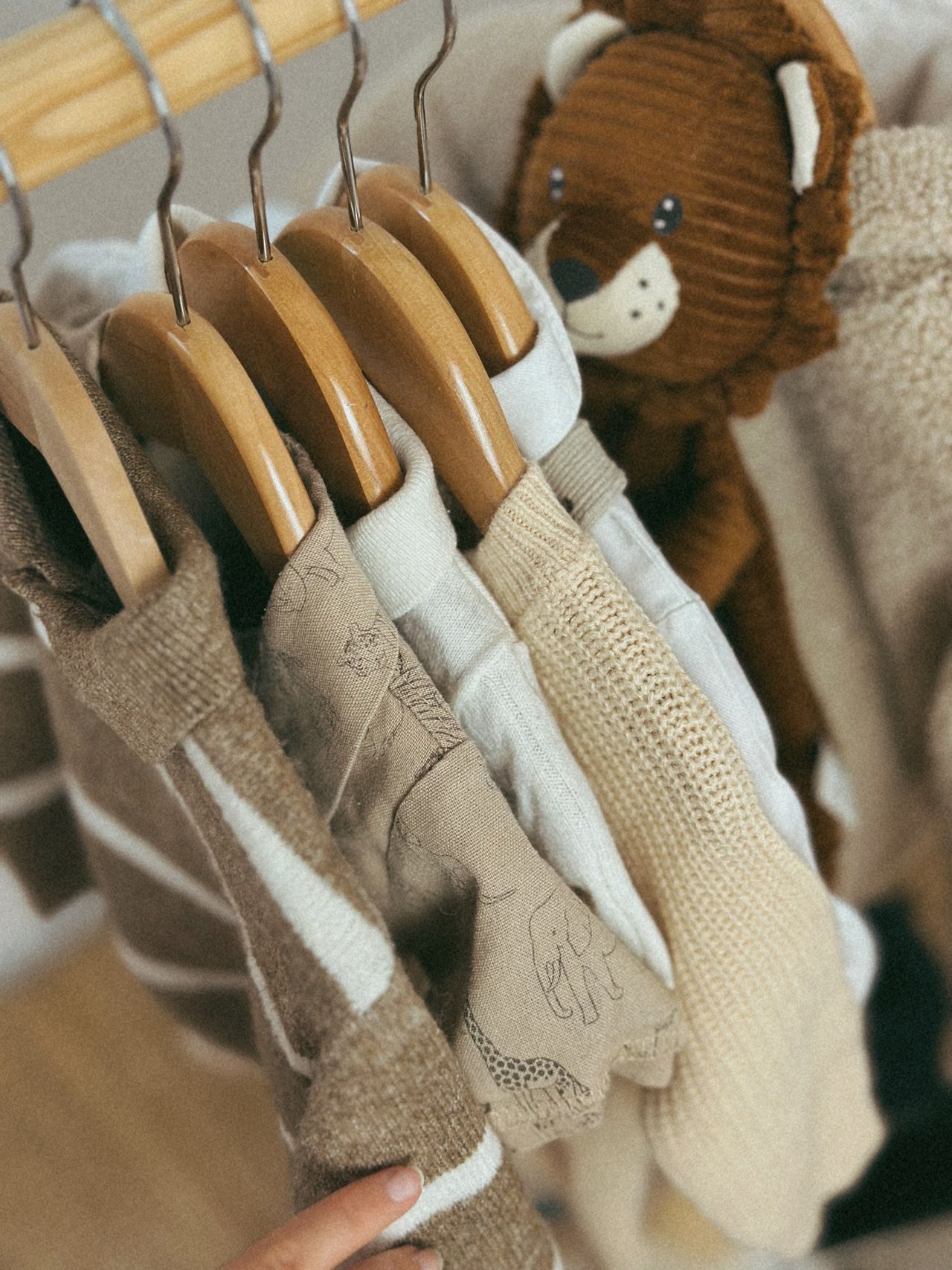 Baby clothes on wooden hangers beside a soft toy